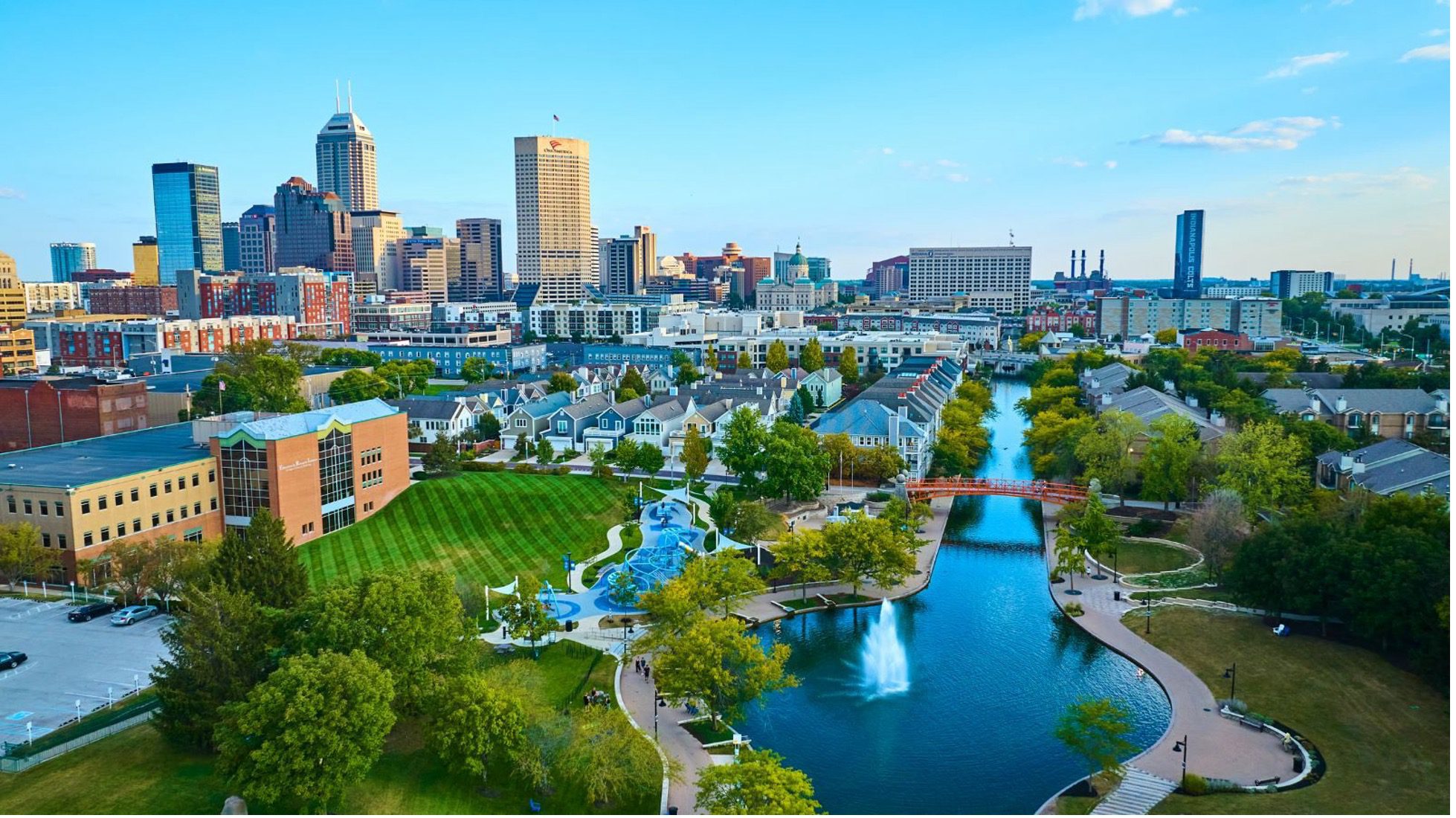 Aerial view of downtown Indianapolis featuring the Canal Walk, green spaces, fountains, and the city skyline in the background