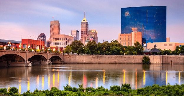 Indianapolis skyline reflected in the White River at sunset with downtown buildings and bridges in view.