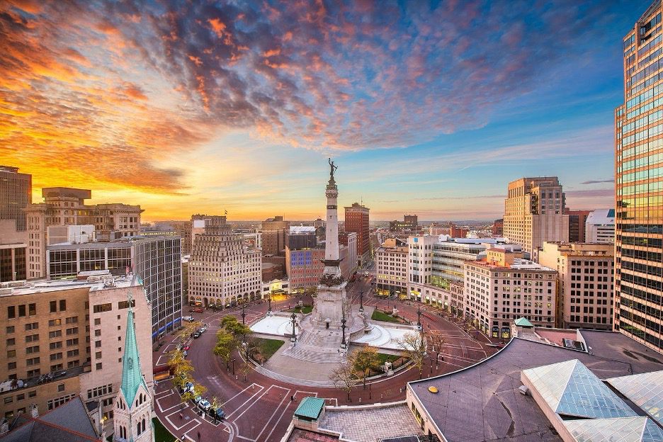 Monument Circle in downtown Indianapolis at sunset with the Soldiers and Sailors Monument surrounded by city buildings.